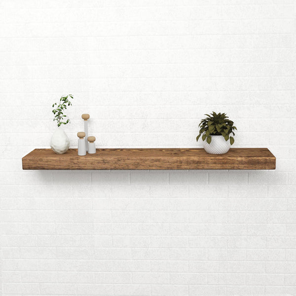 A simple wooden shelf mounted on a white brick wall, displaying a small plant, three white vases, and a small white bowl.