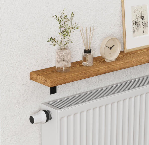 a wooden shelf with a vase of greenery, a clock, and a diffuser on it, placed next to a white radiator.