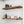 a set of wooden shelves mounted on a white tiled wall, displaying various kitchen items such as bottles, a bowl, and a sugar container.