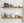 a set of wooden shelves mounted on a white brick wall, displaying various kitchen items such as bottles, bowls, and a teapot.