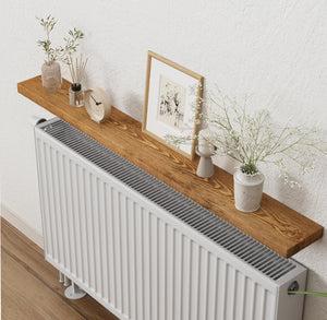 a wooden shelf mounted on a white wall, with a white radiator underneath. On the shelf, there are several decorative items, including a clock, a picture frame, and a vase with flowers.