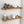 a set of wooden shelves mounted on a white tiled wall, displaying various kitchen items such as bottles, bowls, and a candle.