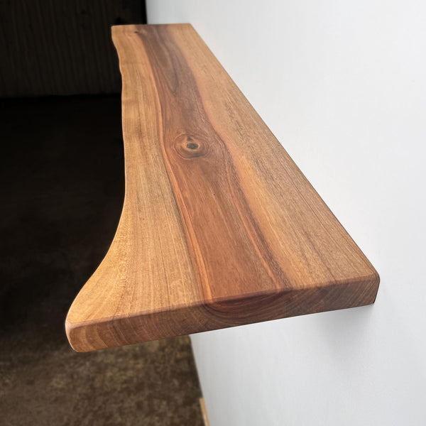 A wooden shelf mounted on a wall, with a natural wood grain texture and a visible knot in the wood.