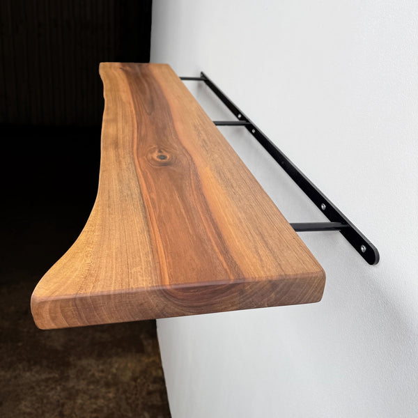 A wooden shelf mounted on a white wall, with a black metal bracket supporting it.