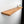 A wooden shelf mounted on a white wall, with a small plant and a white candle placed on it.