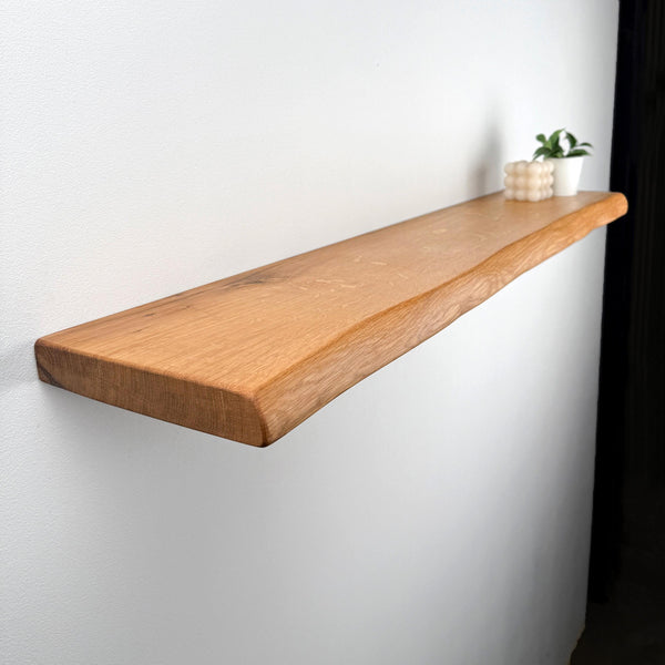 A wooden shelf mounted on a white wall, with a small plant and a white candle placed on it.