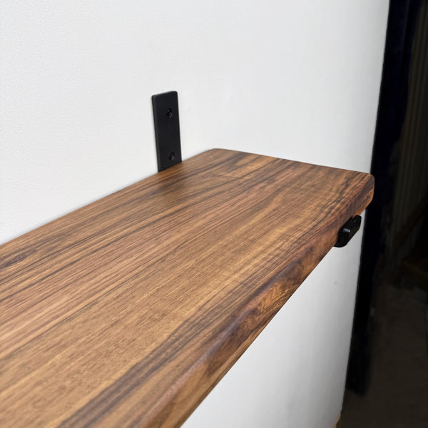 A wooden shelf mounted on a wall, with a black metal bracket attached to the wall.