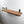 A wooden shelf mounted on a white wall, with two small potted plants placed on it.