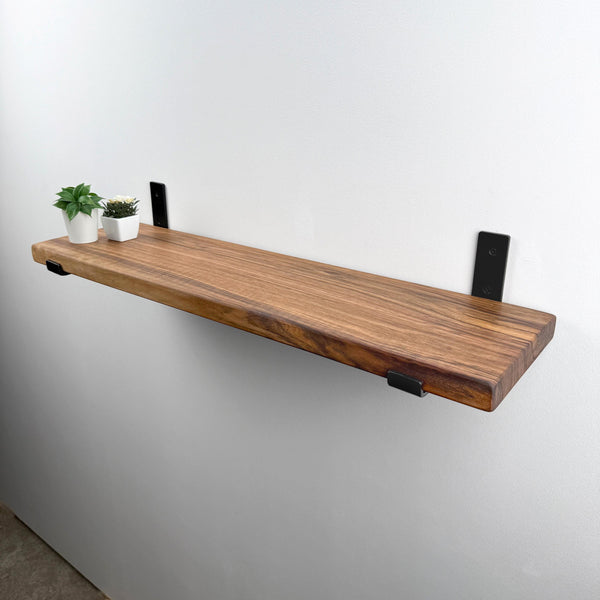 A wooden shelf mounted on a white wall, with two small potted plants placed on it.