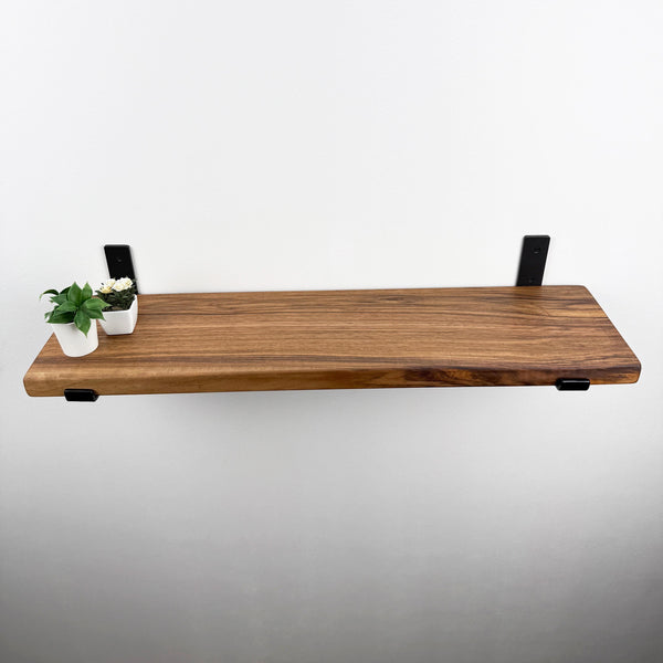 a wooden shelf mounted on a wall, with two small potted plants placed on it.