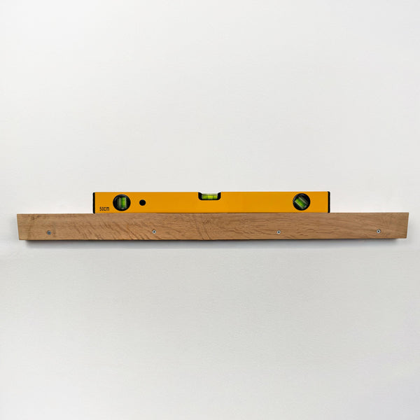 A yellow spirit level is mounted on a wooden shelf against a white wall.
