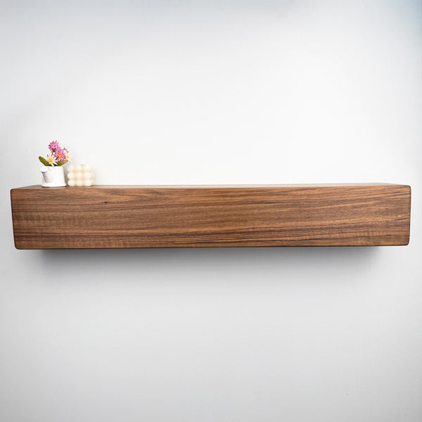 A wooden shelf mounted on a white wall, with a small vase of flowers and a white candle placed on it.