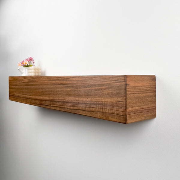 A wooden shelf mounted on a white wall, with a small vase of flowers placed on top of it.