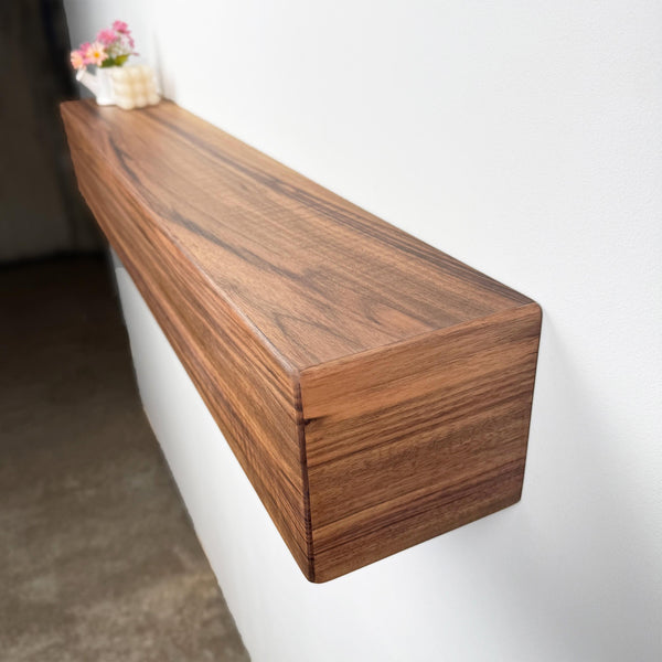 a wooden shelf mounted on a wall, with a vase of flowers placed on top of it.