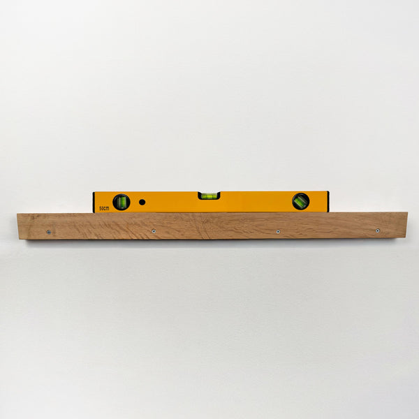 A yellow spirit level is mounted on a wooden shelf against a white wall.