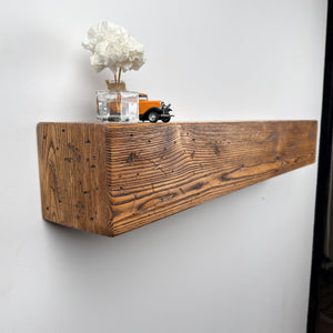 a wooden shelf mounted on a wall, with a vase of white flowers and a small toy truck placed on top of it.