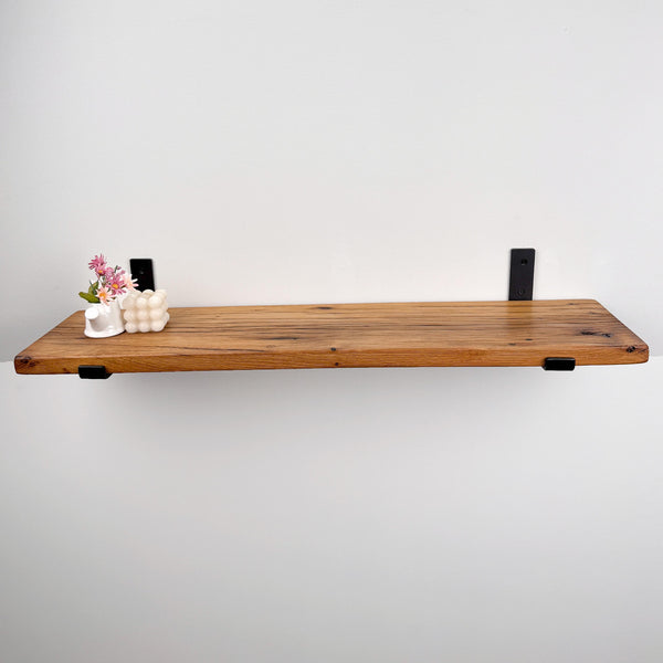 a wooden shelf mounted on a white wall, with a small white vase containing flowers placed on the shelf.