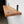 A wooden shelf mounted on a white wall, with a black metal bracket attached to the wall.