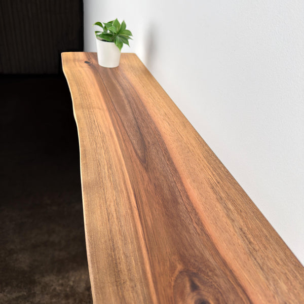 A wooden shelf with a potted plant on top, placed against a white wall.