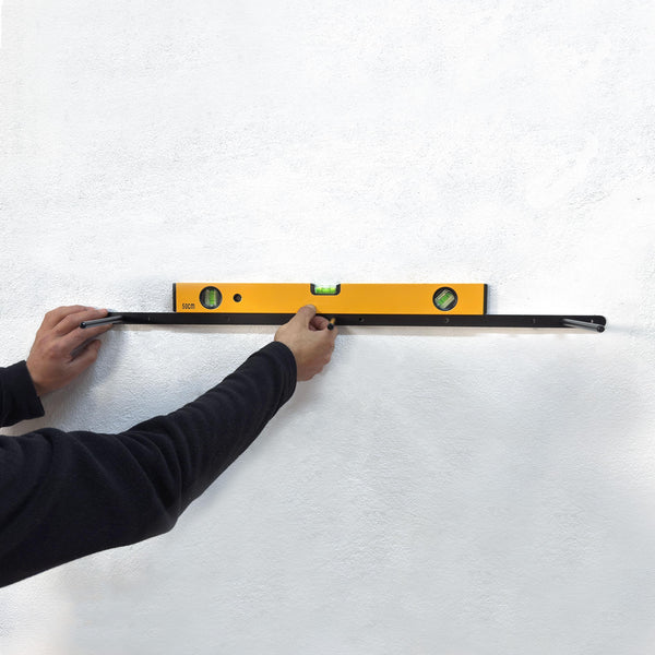 A person's hand is using a yellow level to ensure a shelf is properly mounted on a white wall.
