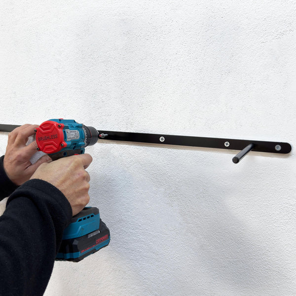 A person is using a power drill to drill a hole in a white wall.