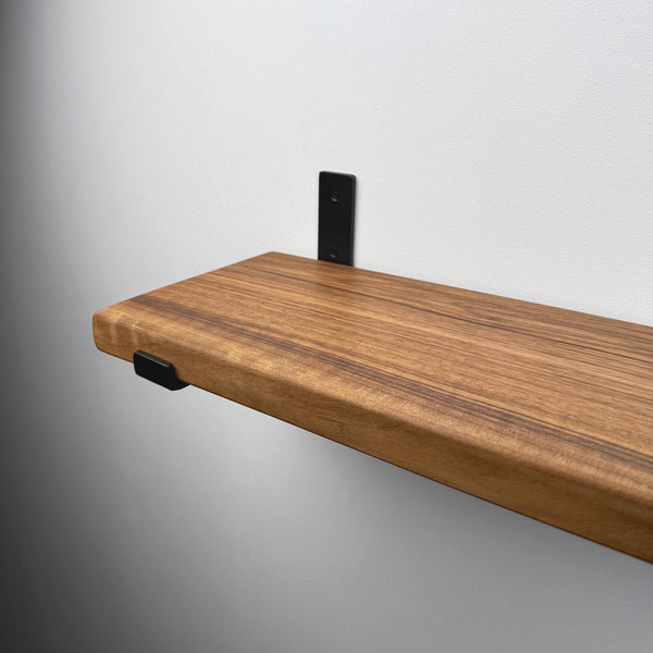 A wooden shelf mounted on a wall, with a black metal bracket attached to the wall.