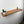 A wooden shelf mounted on a white wall, with a small potted plant and a white cup placed on it.