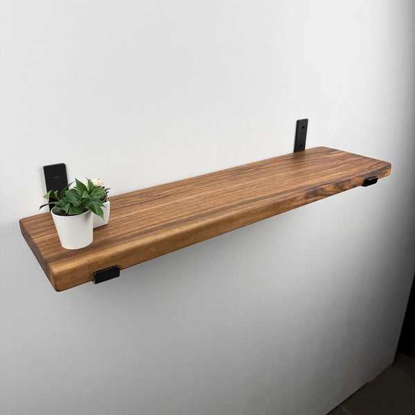 A wooden shelf mounted on a white wall, with a small potted plant and a white cup placed on it.
