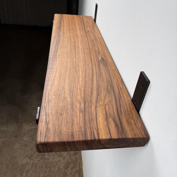 A wooden shelf mounted on a wall, with a dark metal bracket on the right side.