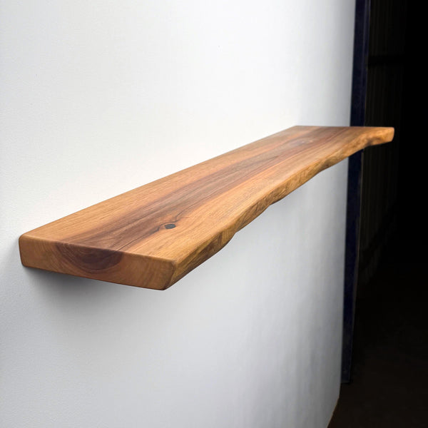 A wooden shelf mounted on a white wall, with a dark background.