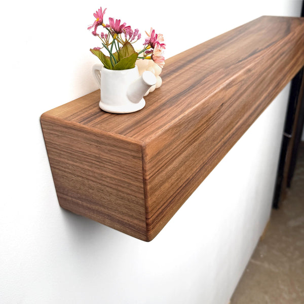 A wooden shelf mounted on a wall, displaying a small white vase with pink flowers and a white teapot.