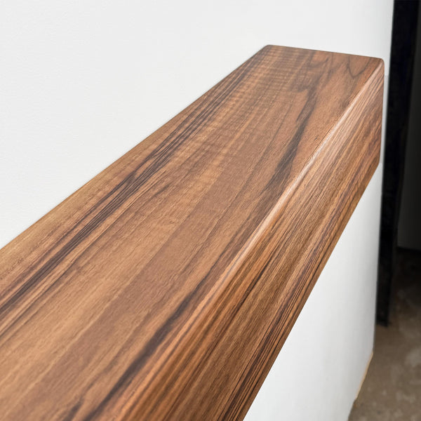 a wooden shelf or ledge with a natural wood grain texture, mounted on a white wall.