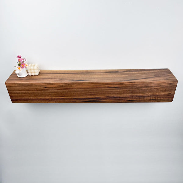a wooden shelf mounted on a white wall, with a small vase of flowers and a white candle placed on it.
