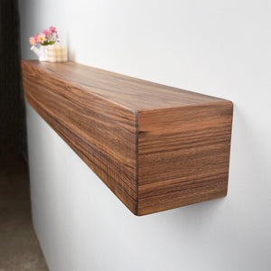 a wooden shelf mounted on a wall, with a vase of flowers placed on top of it.