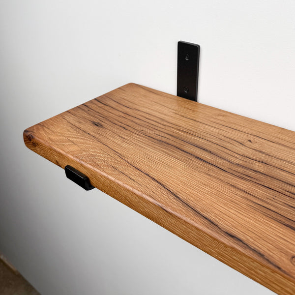 a wooden shelf mounted on a wall, with a black metal bracket attached to the wall.