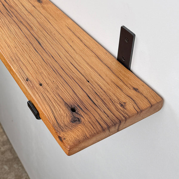 a wooden shelf mounted on a wall, with a black metal bracket attached to the wall.