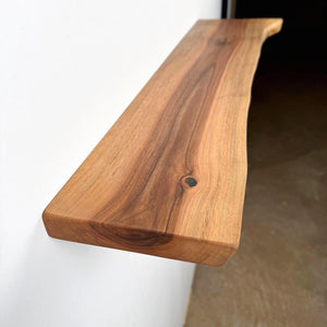 A wooden shelf mounted on a wall, with a natural wood grain texture and a small knot visible on the surface.