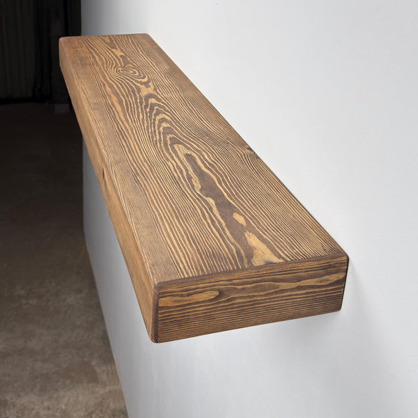 a wooden shelf mounted on a wall, with a dark brown, textured finish.