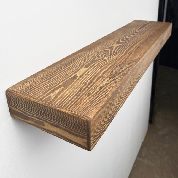 A wooden shelf mounted on a white wall, with a dark brown, weathered appearance.