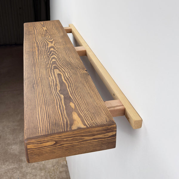 a wooden shelf mounted on a wall, with a dark-colored wooden plank and a light-colored wooden support beam.
