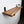 A wooden shelf mounted on a white wall, with a small plant on the shelf and a black metal bracket on the wall.