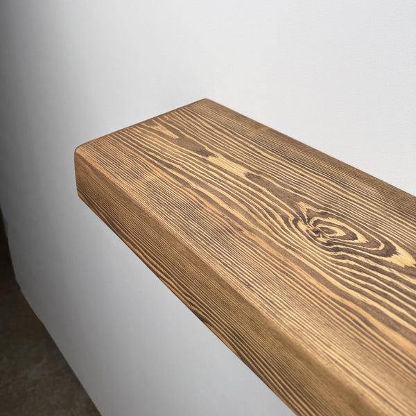 a wooden shelf or ledge with a natural wood grain texture, mounted on a white wall.