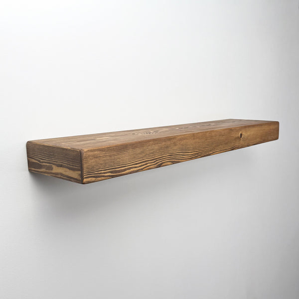 A simple, rectangular wooden shelf mounted on a white wall.